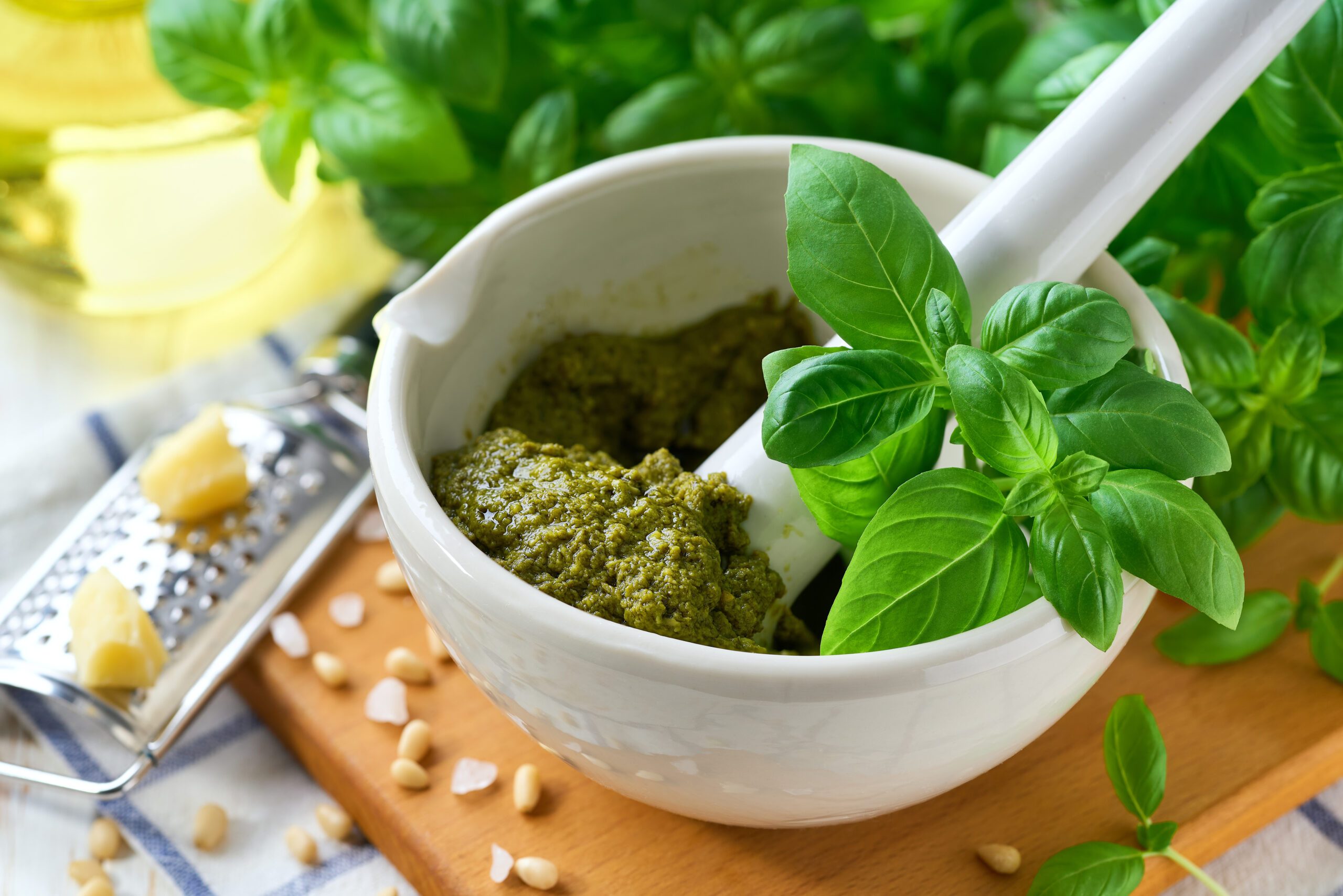 White mortar full of basil pesto, pine nuts ans basil leaves on wooden table,traditional italian pesto recipe for pasta.